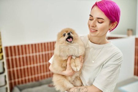lächelnde Tierpflegerin hält schläfrige und gähnende Hündchen in einladendem Haustierhotel, hundefreundliches Konzept