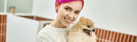 joyful purple-haired dog sitter with cute pomeranian spitz looking at camera in pet hotel, banner
