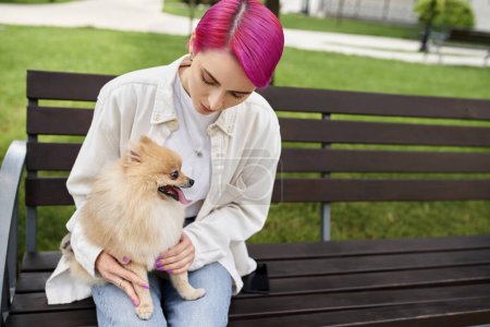Frau mit trendiger Frisur sitzt auf Bank im Park mit entzückender Pommernspitze, Hundeliebhaberin