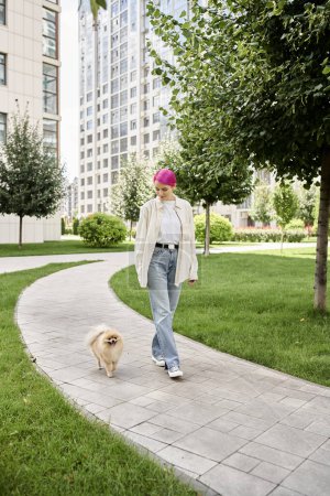 Téléchargez les photos : Pleine longueur de femme aux cheveux violets élégant marchant avec spitz poméranien sur la rue urbaine, la vie de la ville - en image libre de droit