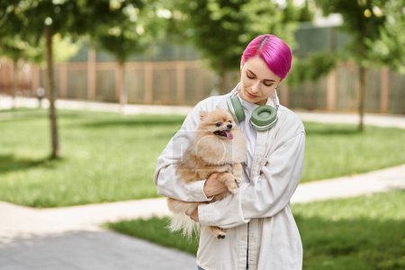 loving pet owner with purple hair and headphones walking with loveable pomeranian spitz in hands