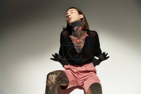 Téléchargez les photos : Beau jeune homme avec des tatouages et piercing posant sur le sol avec les yeux fermés, concept de mode - en image libre de droit