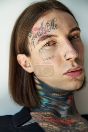 Téléchargez les photos : Portrait de sexy bel homme avec des tatouages sur son visage en regardant la caméra sur fond gris, mode - en image libre de droit
