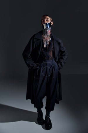 vertical shot of young man in futuristic laced mask and in black stylish outfit, looking at camera
