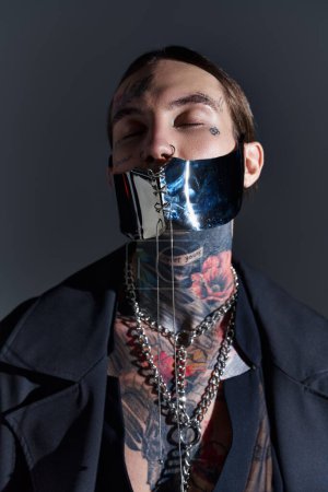 Téléchargez les photos : Portrait d'homme séduisant en masque futuriste noir posant les yeux fermés, concept de mode - en image libre de droit