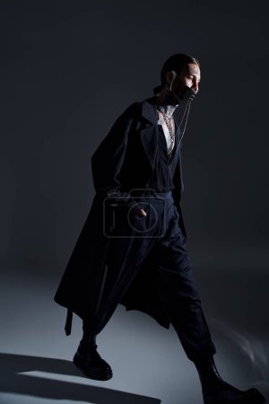 vertikale Aufnahme eines stilvollen Mannes in schwarzer futuristischer Kleidung mit Accessoires, der spazieren geht und wegsieht