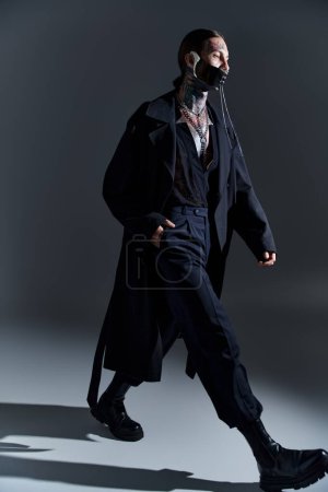 junger sexy Mann in futuristischer schwarzer Kleidung und Schnürmaske, der mit der Hand in der Tasche geht, Mode
