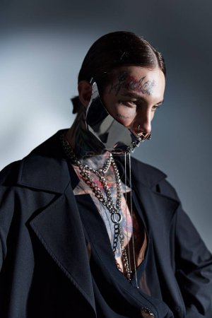 vertical shot of young good looking man in stylish black attire with futuristic laced mask, fashion