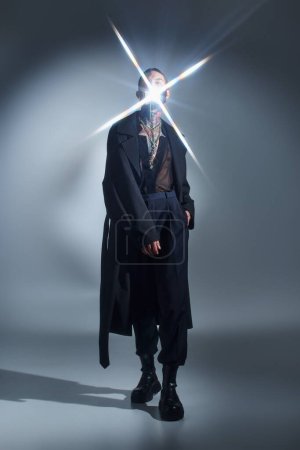 junger Mann in schwarzer futuristischer Kleidung posiert mit Lichtfunken im Gesicht, Modekonzept