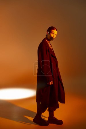 good looking young man posing in black futuristic attire surrounded by orange light, fashion concept