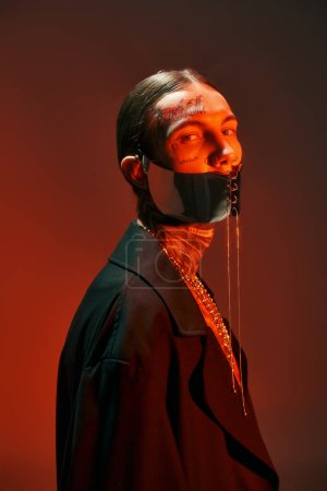 portrait of stylish alluring man with tattoos and futuristic laced mask looking at camera, fashion