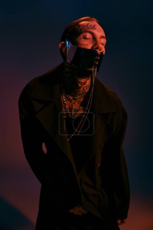 handsome stylish man with tattoos and laced dystopian mask posing with closed eyes, fashion concept