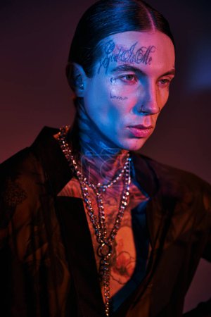 vertical shot of handsome young man with tattoos and chain accessories looking away, fashion concept