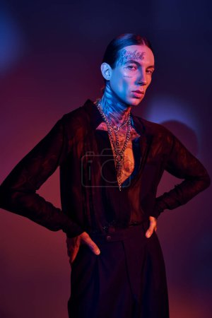 alluring young man with tattoos in transparent shirt posing with hands on hips, fashion concept