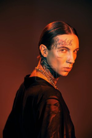 handsome young man in black attire with tattoos turning his head and looking at camera, fashion