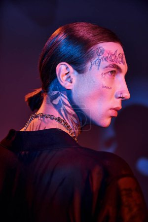 Téléchargez les photos : Portrait de jeune homme sexy avec des tatouages posant de profil avec de la lumière sur le visage, concept de mode - en image libre de droit