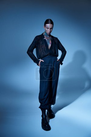 Photo for Vertical shot of young sexy male model in black attire with hands in pockets looking down, fashion - Royalty Free Image