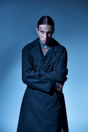 Téléchargez les photos : Beau jeune homme tatoué et percé enveloppant dans son manteau noir en regardant la caméra, la mode - en image libre de droit