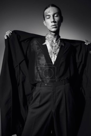 black and white photo of stylish man with tattoos in transparent shirt with coat, fashion concept