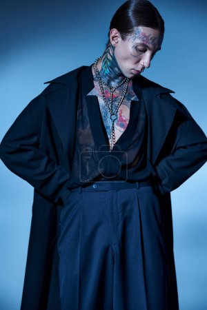 Téléchargez les photos : Plan vertical de jeune homme élégant en tenue noire avec des tatouages posant avec les mains sur les hanches, la mode - en image libre de droit