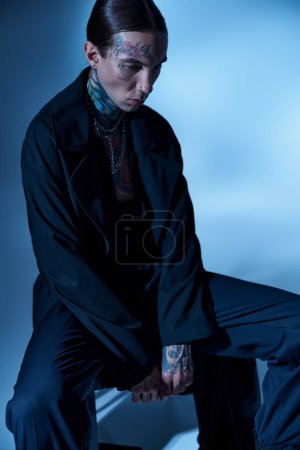 Téléchargez les photos : Plan vertical de beau jeune homme assis sur une chaise en tenue noire et regardant ailleurs, la mode - en image libre de droit
