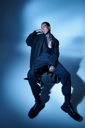 Téléchargez les photos : Plan vertical de l'homme séduisant élégant en tenue noire assis sur une chaise avec les yeux fermés, la mode - en image libre de droit