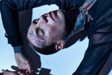 top view of handsome young man with tattoos lying with closed eyes with hands raised to face