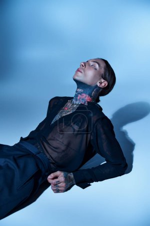 sexy stylischer Mann mit Tätowierungen im transparenten Hemd mit geschlossenen Augen auf dem Boden liegend, Modekonzept