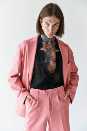 guapo modelo masculino elegante con tatuajes en chaqueta rosa con las manos en los bolsillos, concepto de moda
