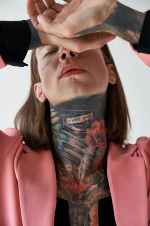 Foto de Tiro vertical de joven hombre guapo con tatuajes con las manos cerca de la cara y los ojos cerrados, la moda - Imagen libre de derechos
