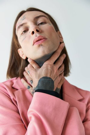 stylish young male model with tattoos in pink blazer looking at camera with hands on neck, fashion magic mug #679133624
