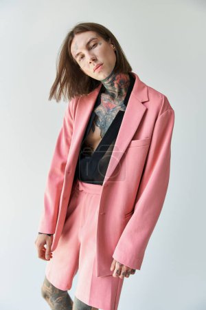 handsome young man with tattoos in stylish pink blazer and shorts looking at camera, fashion concept