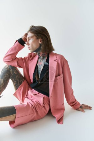 Foto de Tiro vertical de hombre sexy guapo con tatuajes sentados en el suelo y mirando hacia otro lado, concepto de moda - Imagen libre de derechos