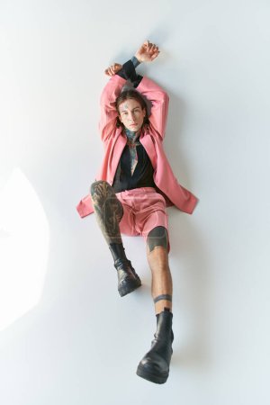 Foto de Vista superior de hombre sexy con estilo en chaqueta rosa y pantalones cortos acostado con las manos levantadas, concepto de moda - Imagen libre de derechos