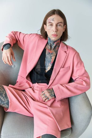 stylish sexy man in pink blazer and shorts sitting on chair looking at camera, fashion concept