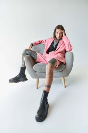 Téléchargez les photos : Beau jeune homme en blazer rose élégant et court assis sur la chaise en regardant la caméra, la mode - en image libre de droit