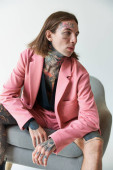 vertical shot of alluring young man with tattoos relaxing on chair and looking away, fashion concept puzzle #679134330
