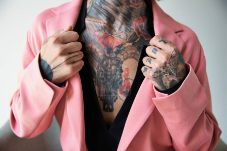 Téléchargez les photos : Vue recadrée du jeune homme avec des tatouages avec les mains sur le col de son élégant blazer rose, mode - en image libre de droit