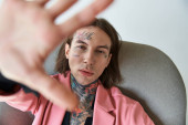 stylish young man with tattoos and piercing in pink blazer with hand in front of camera, fashion puzzle #679134440