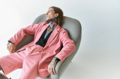 sexy young man in stylish pink outfit relaxing on comfy chair and looking away, fashion concept Poster #679134490