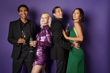 Christmas party, happy multiethnic couples in festive attire holding glasses of champagne on purple