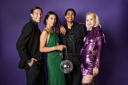 Nouvel An 2024, groupe d'amis interracial joyeux en costumes et robes debout avec ballon disco