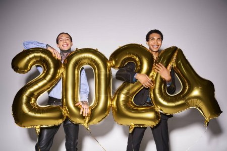 happy interracial male friends holding balloons with 2024 numbers during party, New Year concept