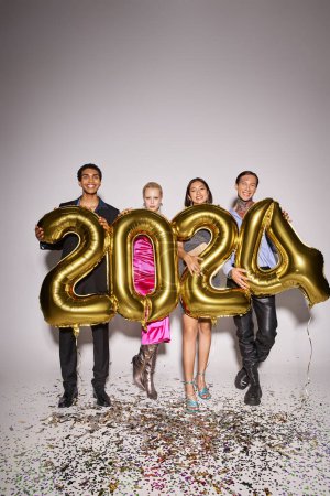 vier glückliche interrassische Freunde halten Luftballons mit 2024 Zahlen in der Nähe von Konfetti, Neujahrsparty
