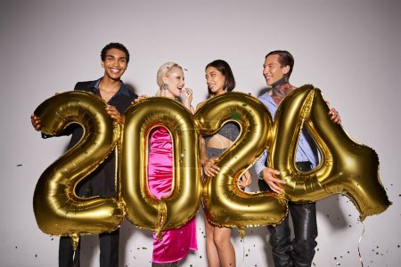 joyful interracial friends holding balloons with 2024 numbers near falling confetti, New Year party