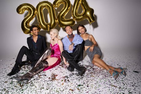 personas multiculturales felices sentados cerca de confeti y globos con 2024 números, Feliz Año Nuevo