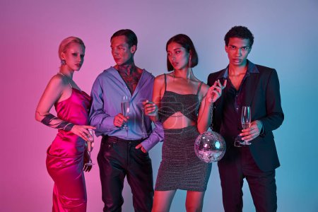 Foto de Grupo de amigos multiculturales sosteniendo copas de champán y bola disco sobre fondo rosa púrpura - Imagen libre de derechos