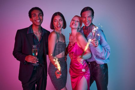 happy multiethnic friends holding sparklers and champagne, celebrating Christmas on purple pink