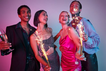 Happy New Year, joyful four multiethnic friends holding sparklers and champagne on purple pink