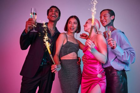 Celebración de Año Nuevo, alegres cuatro amigos multiétnicos sosteniendo bengalas y champán en rosa púrpura